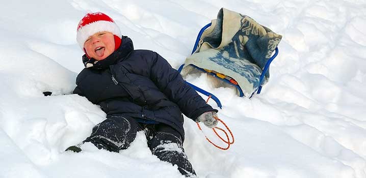 Lille dreng griner i sneen efter at være faldet af slæden