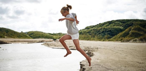 Pige springer i vandet tæt på sol og strand