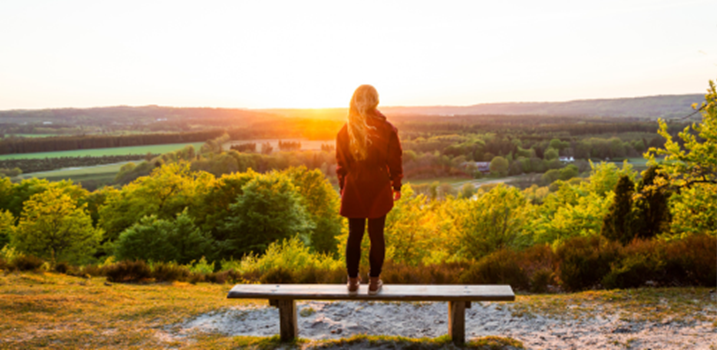 kvinde står på bænk i solskin og kigger ud over efterårslandskabet